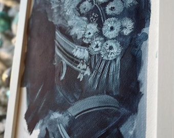 May include: A framed watercolor painting featuring a bouquet of white flowers in a dark blue vase. The artwork is rendered in shades of blue and white, with visible brushstrokes. The frame is white, and the painting is displayed at an angle.