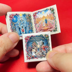 May include: A miniature book titled The Nutcracker and the Mouse King by E.T.A. Hoffmann. The cover features a colorful illustration of a nutcracker and a mouse king. The open pages display detailed scenes of a character and a candy-themed landscape.