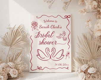 Könnte beinhalten: Ein rechteckiges Schild mit burgunderfarbenem Text und Illustrationen, darunter Schwäne, Tauben und florale Elemente. Auf dem Schild steht "Welcome to Sarah Clark's Bridal shower" und ein Datum. Das Schild ist von Trockenblumen umgeben.