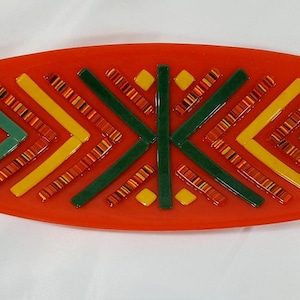 May include: An oval-shaped serving tray with a geometric design. The tray is made of glass and features a red background with green, yellow, and orange accents.