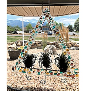 May include: A triangular glass planter with a mosaic of colorful glass pieces. The planter has three hooks for hanging and is filled with three air plants.
