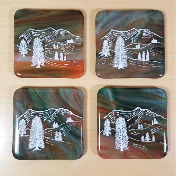 Fused glass coasters in streaky green and burnt orange with hand-drawn mountain scene in white enamel