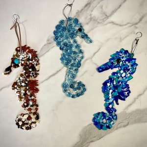 May include: Three glass seahorse ornaments, each with a different color and pattern. One is brown with white and tan accents, one is blue with white and turquoise accents, and one is light blue with white accents.