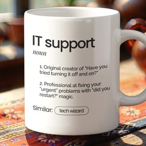 Könnte beinhalten: Weißer Keramikbecher mit dem Text "IT support" und einer Definition. Die Definition enthält Sätze wie "Haben Sie versucht, es aus- und wieder einzuschalten?" und "Haben Sie neu gestartet?" Auf dem Becher steht auch das Wort "tech wizard".