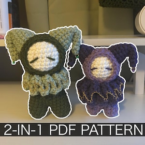 May include: Two handmade crochet dolls in the image. One doll is green and the other is purple. Both dolls have white faces with closed eyes and are wearing jester-style hats. The text "2-IN-1 PDF PATTERN" is at the bottom of the image.