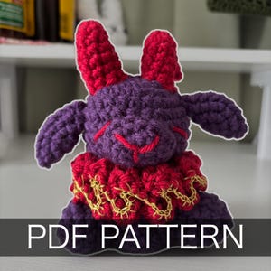 May include: A handmade crochet bunny in purple and red. The bunny has large red ears, purple arms, and a red smile. It wears a red ruffled collar with gold accents. The text "PDF PATTERN" is displayed at the bottom.