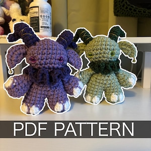 May include: Two crocheted plush figures, one purple and one green, with horns, large ears, and white-tipped feet. The purple figure has a dark purple ruffled collar and pink eyes. The green figure has a dark green collar and yellow eyes. The text "PDF PATTERN" is at the bottom.