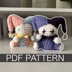 Puede incluir: Dos muñecos bufones de ganchillo con gorros puntiagudos y dijes en forma de estrella. El muñeco de la izquierda tiene hilo rosa, azul y amarillo pastel. El de la derecha es de hilo morado oscuro y blanco con ojos en cruz. Texto PDF PATTERN.