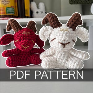 May include: Two crocheted goat figurines, one red and one white, with brown horns and gold accents. The red goat has gold stitching on its face. The white goat has brown stitching. The text "PDF PATTERN" is at the bottom.