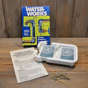 May include: A vintage Water Works board game box with the game title in white and yellow. The box features images of pipes and plumbing fixtures. The game includes cards, a white plastic tray, and a manual. Ages 8 to Adult, 2 to 5 Players.