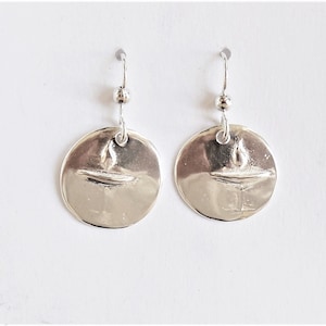 May include: A pair of silver dangle earrings with a round disc pendant featuring a textured design. The earrings have a simple hook closure.