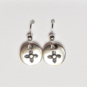 May include: Silver dangle earrings with a circular charm featuring a stylized cross design.