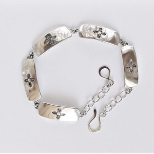 Puede incluir: Pulsera de plata con cierre de cadena y cinco dijes rectangulares con un diseño estilizado. Cada dije tiene una textura martillada.