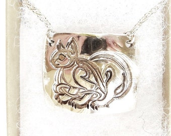 May include: A silver necklace with a pendant featuring a detailed, stylized squirrel design. The pendant is rectangular and has a slightly rounded shape.