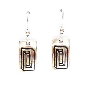 May include: A pair of silver earrings with a geometric design. Each earring features a rectangular pendant with a black outline of a three-dimensional shape.
