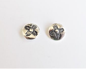 May include: A pair of silver earrings with a circular design featuring a stylized four-pointed star.