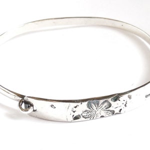 May include: A silver bangle bracelet with a floral design and a clasp. The bracelet is about 6 inches in diameter.