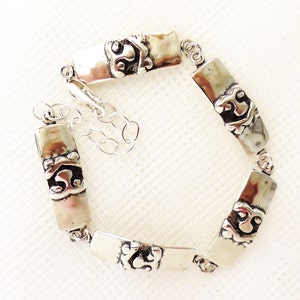 May include: Silver bracelet with a chain and rectangular links featuring a decorative design.