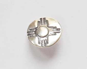 May include: A silver charm with a stylized sun symbol, known as the Zia symbol, in a black outline.