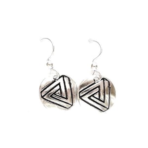 May include: A pair of silver-toned earrings. Each earring features a circular pendant with a black and silver impossible triangle design. The earrings have a simple hook closure and are set against a white background.