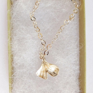 May include: A gold chain necklace with a delicate pendant shaped like a ginkgo leaf.