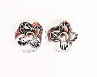 May include: A pair of silver earrings with a stylized sun symbol design. The earrings are round and have a smooth, polished finish.