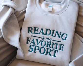 May include: Gray sweatshirt with the text "Reading is my favorite sport" embroidered in teal.