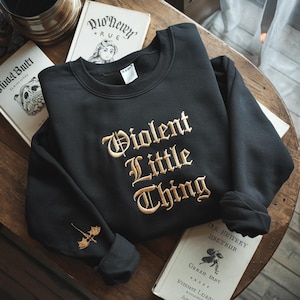 May include: Black sweatshirt with a gold embroidered design that reads "Violent Little Thing".