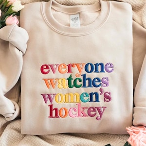 K&ouml;nnte beinhalten: Beiges Sweatshirt mit dem gestickten Text "everyone watches women's hockey" in Regenbogenfarben. Das Sweatshirt mit Rundhalsausschnitt ist aus weichem Material und f&uuml;r den Freizeitgebrauch geeignet.