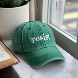 May include: A green baseball cap with the word "resist" embroidered in white on the front.
