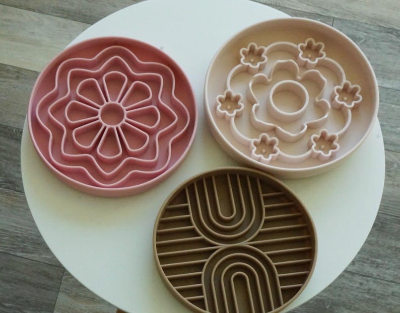 K&ouml;nnte beinhalten: Drei runde Futtern&auml;pfe f&uuml;r Haustiere in Rosa- und Braunt&ouml;nen. Die N&auml;pfe haben einzigartige Designs, darunter eine Blume und ein Regenbogenmuster. Die N&auml;pfe sind aus einem strapazierf&auml;higen Material gefertigt und sollen das Fressen verlangsamen.