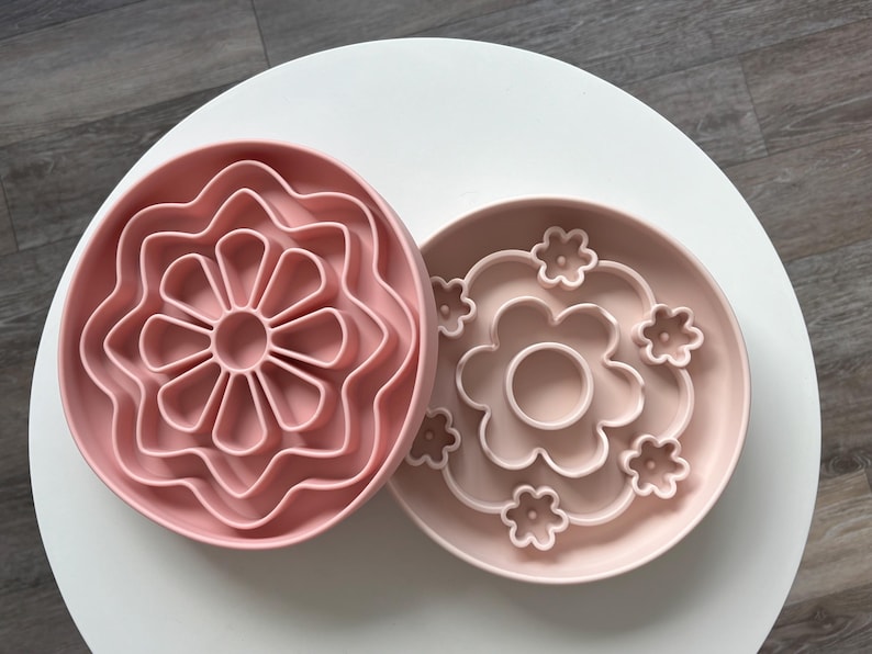 K&ouml;nnte beinhalten: Zwei rosa, bl&uuml;tenf&ouml;rmige Silikon-Slow-Feeder-Schalen. Eine Schale hat ein mehrbl&auml;ttriges Design, die andere einen Blumenumriss mit kleineren Blumenakzenten. Die Schalen sollen das Fressen von Haustieren verlangsamen.