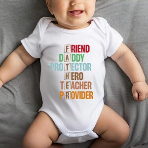 May include: White baby bodysuit with the words "FRIEND, DADDY, PROTECTOR, HERO, TEACHER, PROVIDER" in a colourful, stacked design. The text is in a variety of colours, including red, green, blue, brown, and orange. The bodysuit is on a baby.