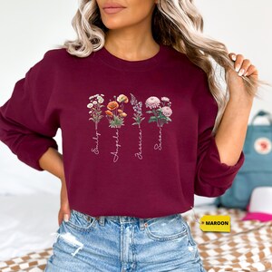 a woman wearing a maroon sweatshirt with flowers on it