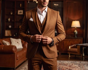 Puede incluir: Un traje marrón de tres piezas con camisa blanca y pañuelo de bolsillo. El traje es entallado y se lleva con un reloj de pulsera negro. El fondo incluye un sofá de cuero, una alfombra estampada y una lámpara de araña.