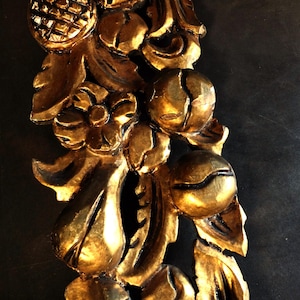 Puede incluir: Un elemento decorativo de madera pintado en oro con intrincados tallados de hojas, flores y frutas. El diseño recuerda a una guirnalda floral o un borde decorativo.