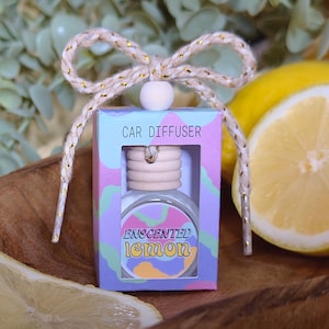May include: A small, white box with a colourful design and the text "CAR DIFFUSER" and "ESSENTIAL LEMON". The box contains a small, clear glass bottle with a wooden cap and a string for hanging.