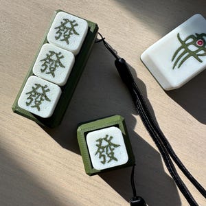 May include: Three green and white mahjong tiles with the Chinese character for 'wind' on them, and a green and white mahjong tile with a green dragon design. The tiles are on a wooden surface.