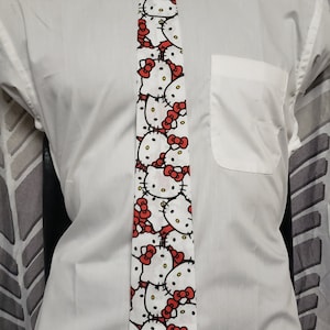 Peut inclure: Une chemise blanche avec une cravate blanche et rouge à motif répété de visages de Hello Kitty.