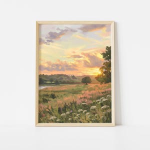 Op de afbeelding: Een ingelijste verticale kunstdruk van een landschap bij zonsondergang. De scène toont een grasweide met witte wilde bloemen op de voorgrond, een verre rij bomen en een gouden lucht vol zachte wolken boven de horizon.