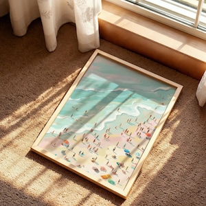 May include: A framed art print depicting a beach scene with people, umbrellas, and waves. The artwork features a light wooden frame and a colorful illustration of a sunny beach day. The print is lying on a brown carpet near a window.