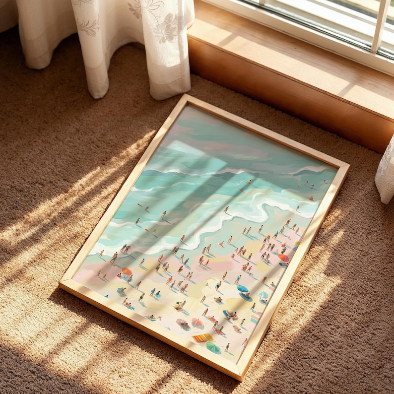May include: A framed art print depicting a beach scene with people, umbrellas, and waves. The artwork features a light wooden frame and a colorful illustration of a sunny beach day. The print is lying on a brown carpet near a window.