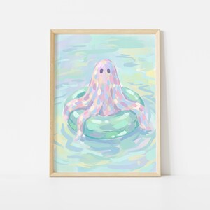 May include: A framed art print featuring a whimsical illustration of a ghost-like figure with pastel colors floating on a green inner tube in water. The ghost has two small black eyes and is surrounded by a light blue and green background.