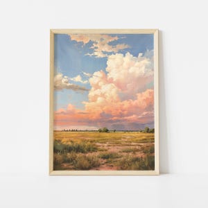 May include: A framed landscape print featuring a vast, open field with dry grasses and low-lying vegetation under a dramatic sky filled with large, billowing clouds tinted in shades of soft pink, peach, and white against a light blue backdrop.