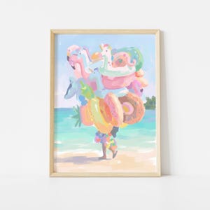 May include: A framed art print depicting a figure carrying a large stack of colorful inflatable pool floats on a beach. The stack includes a pink flamingo, a unicorn, a pineapple, and donut-shaped rings in shades of pink, yellow, and blue.