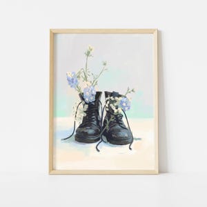 May include: A framed art print featuring a pair of black combat boots filled with blue and white flowers. The boots have black laces and are set against a soft, pastel-colored background. The artwork is a still life with a light wooden frame.