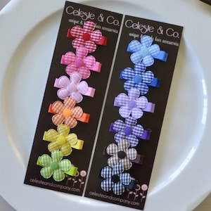 May include: Two dark brown display cards labeled Celeste & Co. each holding six fabric flower hair clips. The clips feature a gingham pattern in various colors including red, pink, orange, yellow, green, blue, purple, brown, and black.