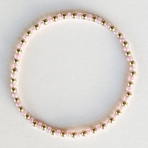 May include: A delicate bracelet made of small pink and gold beads. The bracelet is a simple, elegant design.