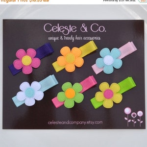 May include: A collection of colorful flower-shaped hair clips. Each clip features a felt flower in shades of pink, orange, blue, green, and yellow, with a contrasting center. The clips are attached to grosgrain ribbon in various colors. The text "Celeste & Co." is visible.