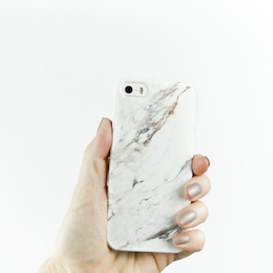 May include: A white iPhone case with a marble pattern. The case has a black camera lens.